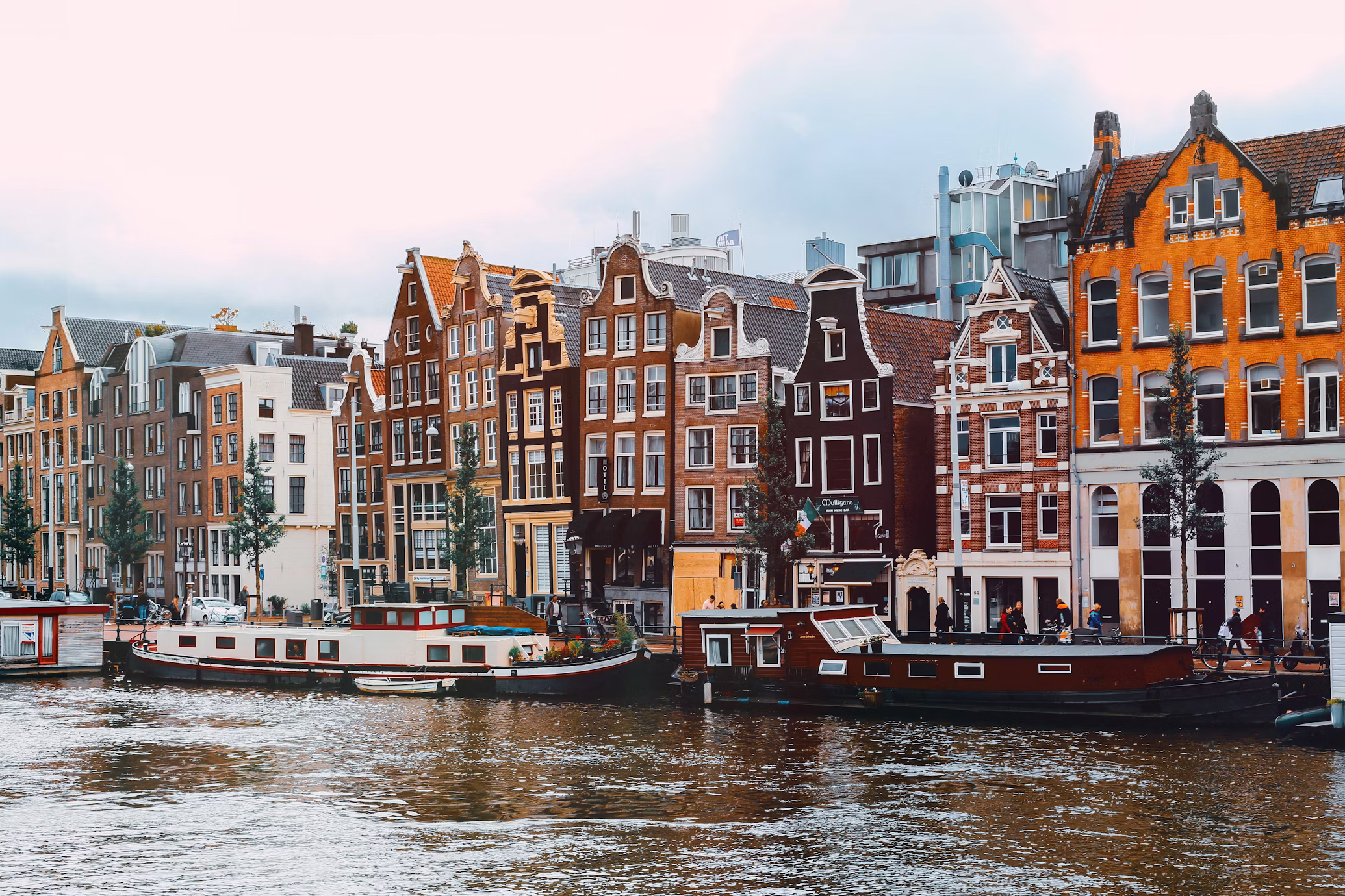 Amsterdam - Traditional tall, narrow brick houses along an Amsterdam canal with green trees and bicycles in the foreground.